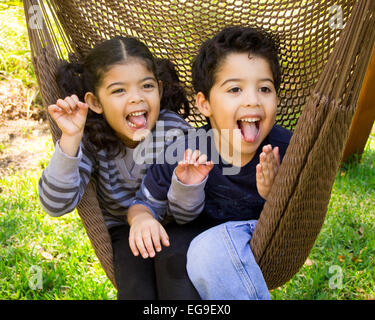 Twin brother and sister sitting in a hammock pulling funny faces