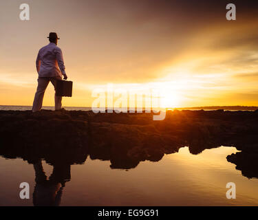Man walking on beach at sunset carrying a suitcase Stock Photo