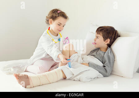 Girl playing nurse to her brother in bed Stock Photo