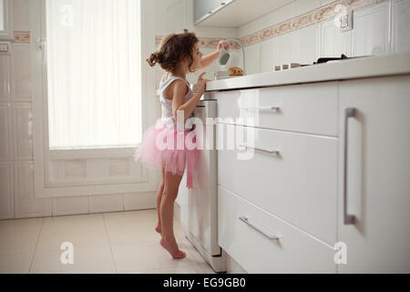 Girl in tutu standing in kitchen pouring milk into a cup Stock Photo