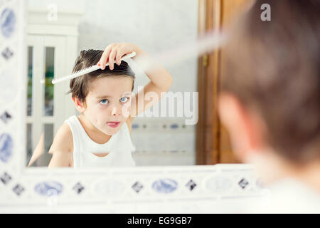 Boy standing in front of a mirror combing his hair Stock Photo