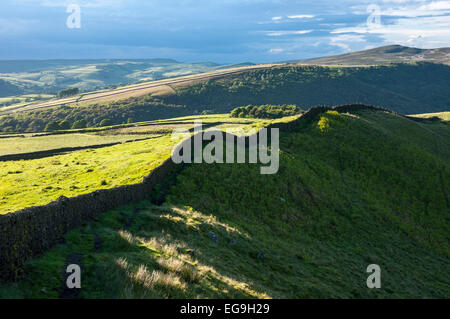 Hills above Hayfield in the Peak District, Derbyshire. A stone wall runs along a ridge with afternoon sunlight on the greens. Stock Photo