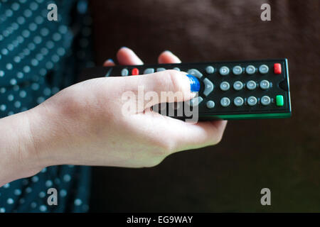a woman changes the tv channel with a remote control in her hand Stock Photo