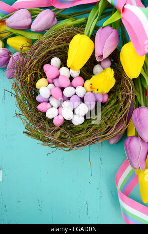 Happy Easter background with painted Easter eggs in birds nest, and yellow and purple silk tulips and ribbon on vintage style ru Stock Photo