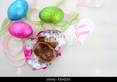 Happy Easter pink, green, and blue foil wrapped chocolate eggs on shabby chic vintage style white wood background. Stock Photo