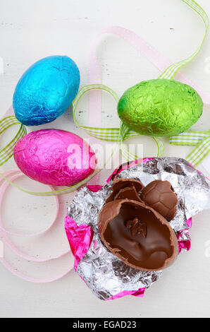 Happy Easter pink, green, and blue foil wrapped chocolate eggs on shabby chic vintage style white wood background, vertical. Stock Photo