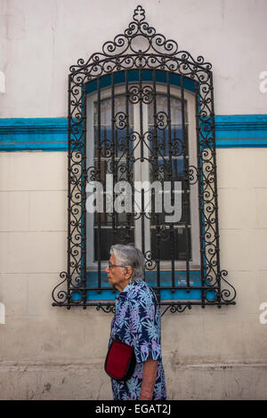 old woman walking past a window of old house with decorative iron grille, Calle San Isidro, Santiago, Chile Stock Photo