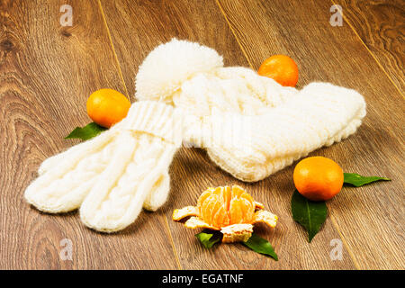 white knitting cap, mittens and tangerines on wooden background Stock Photo