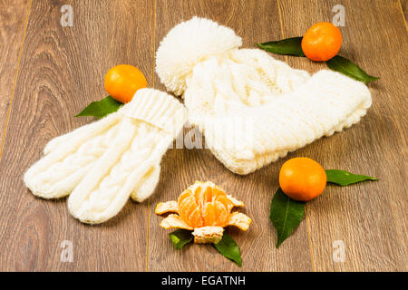 white knitting cap, mittens and tangerines on wooden background Stock Photo