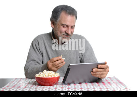 Middle aged man using a tablet computer while eating popcorn at home Stock Photo