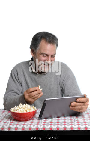 Middle aged man using a tablet computer while eating popcorn at home Stock Photo