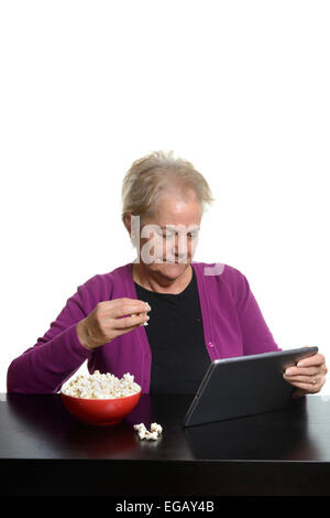 Middle aged woman using a tablet computer while eating popcorn at home Stock Photo