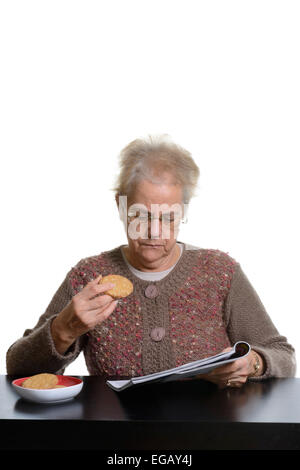 Middle aged woman reading a magazine while eating cookies at home Stock Photo