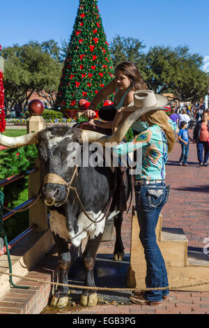 Young woman mounting a bull to have a photo taken, Exchange Avenue, Stockyards District,  Fort Worth, Texas, USA Stock Photo