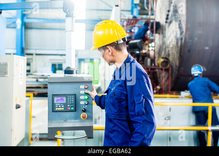 Worker in factory at CNC machine control panel Stock Photo
