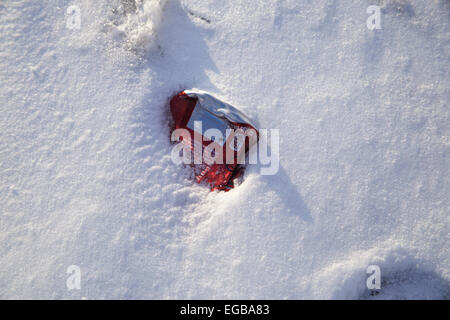 Dr. Pepper soda can on the ground stuck in snow next to foot print. Stock Photo
