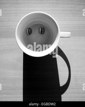 Abstract coffee concept, white empty cup with beans and shadow looks like a funny man character on wooden table Stock Photo