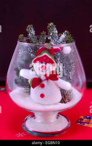 Toy snowman in a glass vase decorated with fir branches on a red tablecloth Stock Photo
