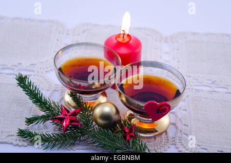 Two golden glasses filled with cognac decorated with a fir branch and a couple of red Christmas stars Stock Photo