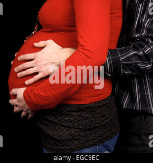 pregnant couple in closeup holding belly over black background Stock Photo