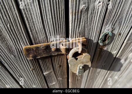 Old and rusty padlock secures an old, weathered wooden door. Stock Photo
