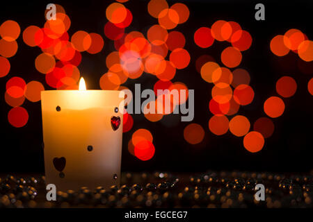 Candle shining placed upon decoration pearls in dark with red bokeh effect Stock Photo