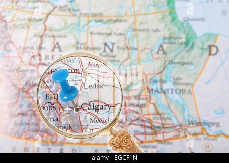 Blue tack on map of central Canada with magnifying glass looking in on Calgary, Alberta Stock Photo