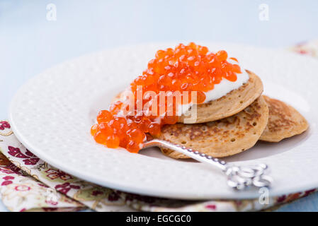 Buckwheat blini with red caviar and sour cream on white plate, selective focus Stock Photo
