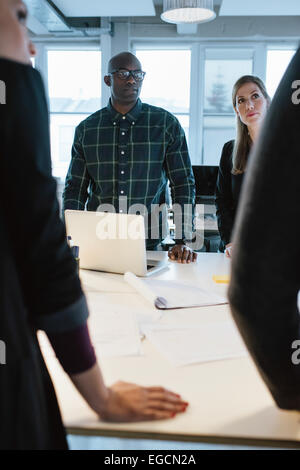 Young people standing at a table discussing work. African man with caucasian woman in office during meeting. Stock Photo