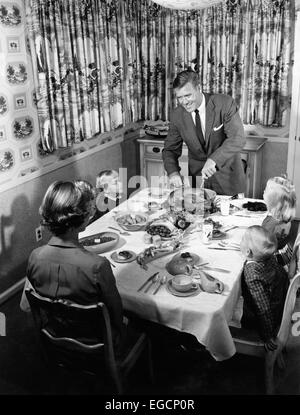 1950s FAMILY OF 5 THANKSGIVING HOLIDAY MEAL MOM DAD MAN WOMAN 3 KIDS BOYS GIRLS AT DINING ROOM TABLE FATHER CARVING TURKEY Stock Photo