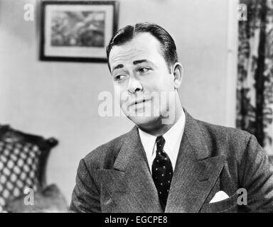 1950s PORTRAIT OF MAN INSIDE LIVING ROOM WEARING SUIT AND TIE LOOKING OFF TO ONE SIDE THINKING CONTEMPLATIVE FUNNY EXPRESSION Stock Photo