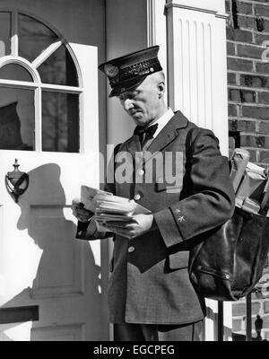1930s 1940s POSTAL SERVICE UNIFORMED MAILMAN DELIVERING MAIL STANDING ON DOORSTEP SORTING LETTERS Stock Photo