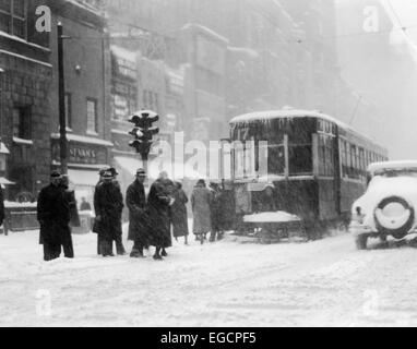 1930s PEDESTRIANS ON SNOW COVERED ICY WINTER STREET IN PHILADELPHIA GETTING ON TROLLEY CAR BY TRAFFIC LIGHT Stock Photo