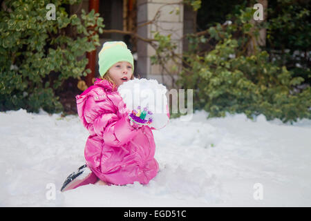 Cute blonde girl holding a huge snowball while sitting in the snow in her backyard in Jerusalem Stock Photo