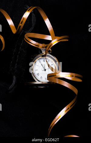 Vintage pocket watch showing five minutes to twelve on black background with golden decoration ribbon (vertical) Stock Photo