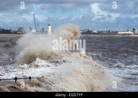 Wild stormy waves crash on the shore with a lighthouse partially obscured in the background under a dark heavy sky Stock Photo