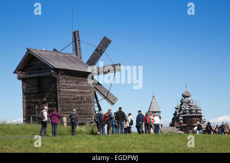 People in front of wooden windmill, belfry and Church of the Intercession of the Virgin and Church of the Transfiguration at Kizhi Pogost in distance, Kizhi Island, Lake Onega, Russia, Europe Stock Photo