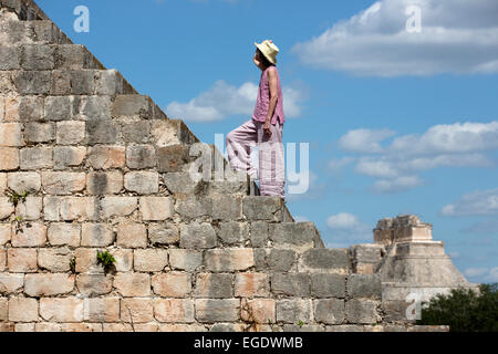 A woman walking up the stairs to the Governors Palace with the Pyramid of the Magician in background Uxmal, Yucatan, Mexico Stock Photo