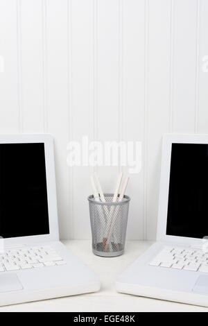 Closeup of two laptops in a white work station with a pencil cup in the middle. The computers are at an angle with blank screens Stock Photo