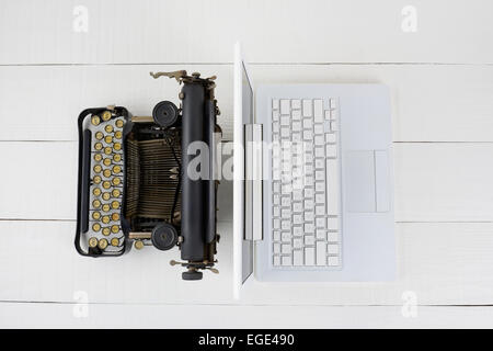 Overhead shot of and old fashioned typewriter back-to-back with a modern laptop computer on a white wood desk. Stock Photo