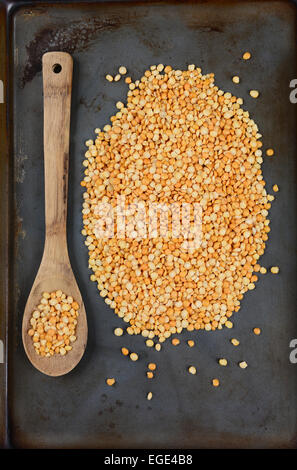 High angle shot of yellow split peas and a wooden spoon on a used metal baking sheet. Vertical Format. Stock Photo