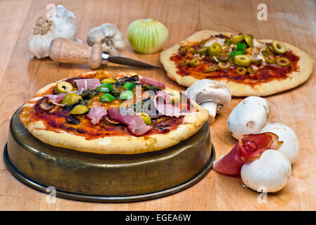 Mini pizzas with prosciutto,mushrooms, olives, pesto and cheese topping surrounded by some of the raw ingredients. Stock Photo