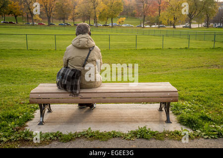 A lonely man sitting on a bench, listening to music, in a park Stock Photo