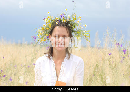 in a lush field girl with a wreath of flowers on her head Stock Photo