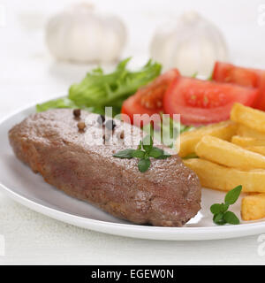 Fried beef steak meat meal with fries, vegetables, tomatoes and lettuce on plate Stock Photo