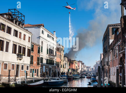 Venice, Italy - 17 February 2015: A Fire fighter helicopter with a waterbag release its load on a house on fire in the Cannaregi Stock Photo