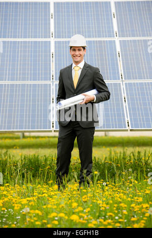Male engineer at solar power station holding blueprints. Stock Photo