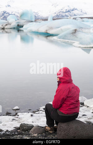 Woman tourist sitting admiring the views at Jokulsarlon Glacial Lagoon, on the edge of Vatnajokull National Park, Iceland in February Stock Photo