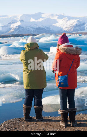Women tourists stood admiring the views at Jokulsarlon Glacial Lagoon, on the edge of Vatnajokull National Park, Iceland in February Stock Photo