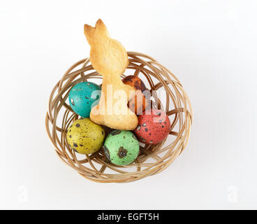 Cookies in the form of an Easter bunny and painted quail eggs in a wicker basket. Top view. Stock Photo